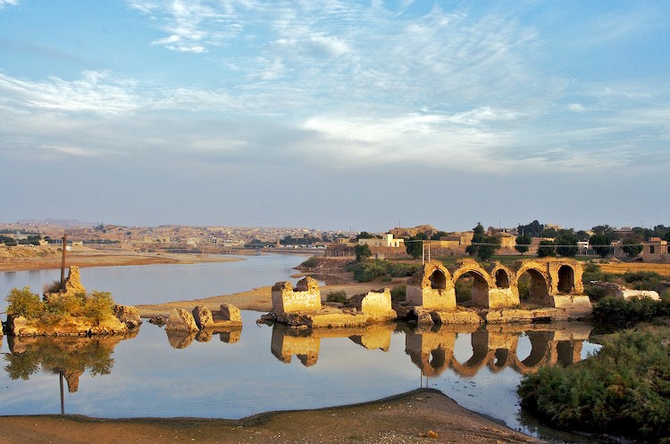 The badly damaged bridge of Band-E-Kaisar. Only three small arches remain. The rest is rubble like  large stones sticking out of the river