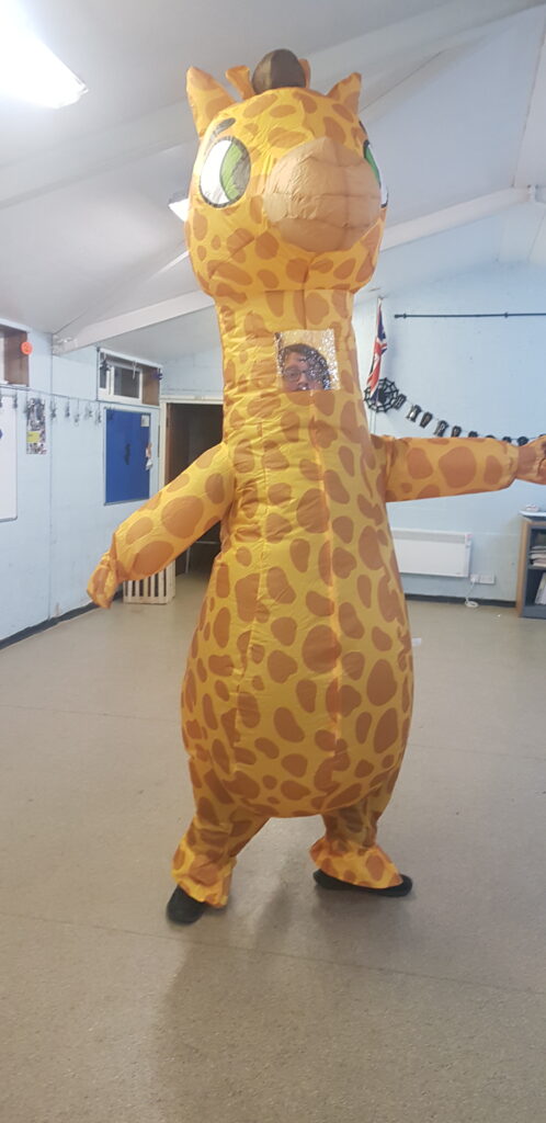 Andy stood in the centre of a small hall dressed in an inflatable giraffe costume with a  small plastic window on the giraffe's neck to see through. 